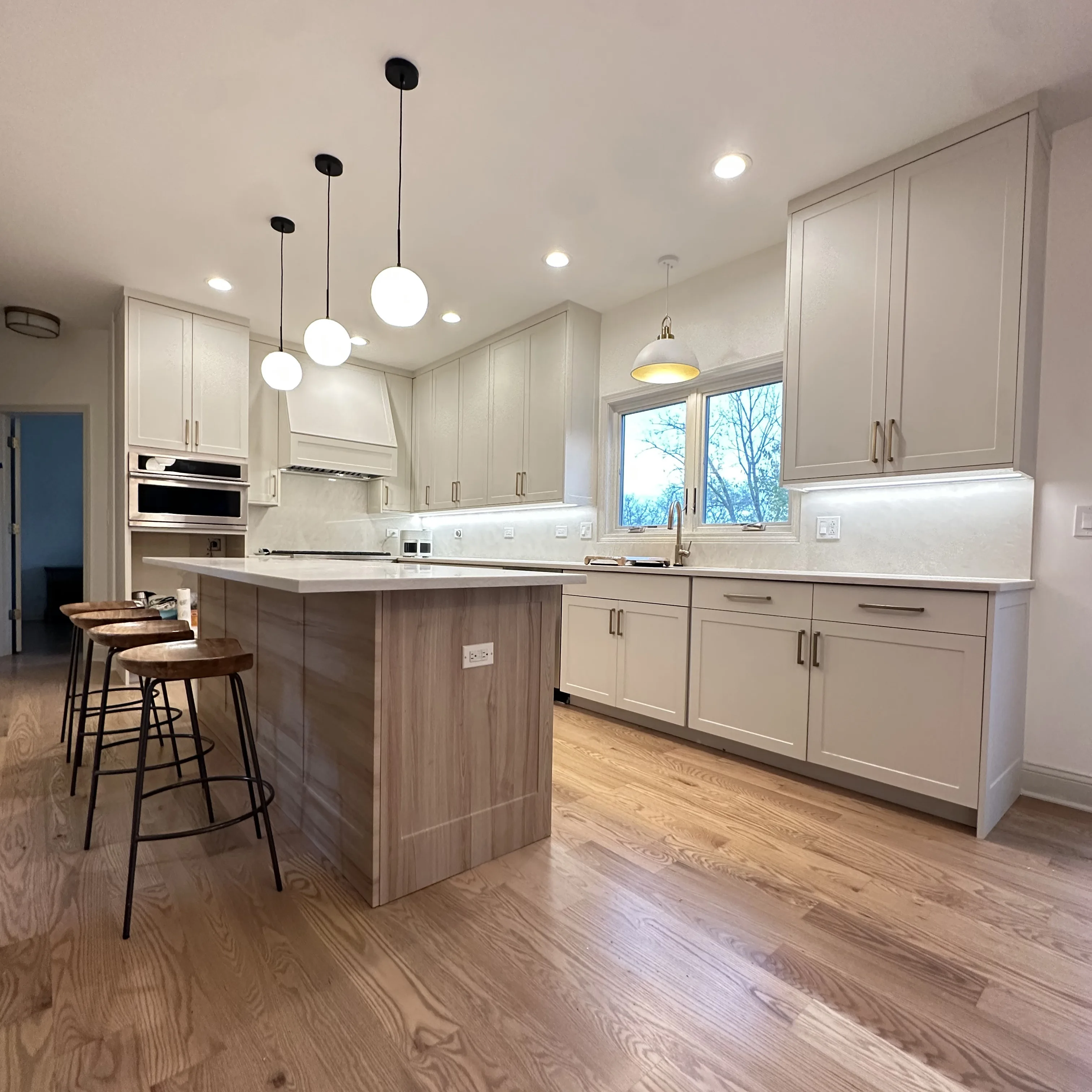 Contemporary kitchen island with bar stools, refinished light-tone oak hardwood flooring, and upgraded pendant lighting as part of Aromark’s full kitchen renovation in Naperville.